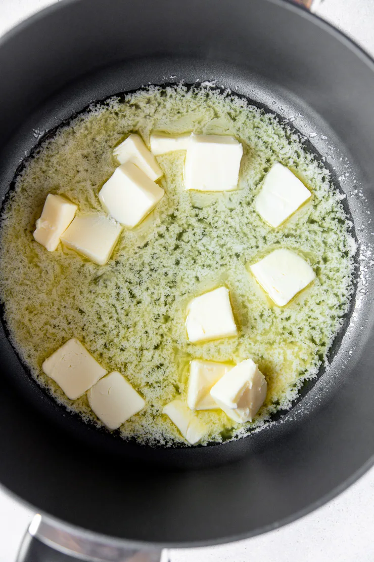 A dark grey pot that is filled with knobs of melting butter.