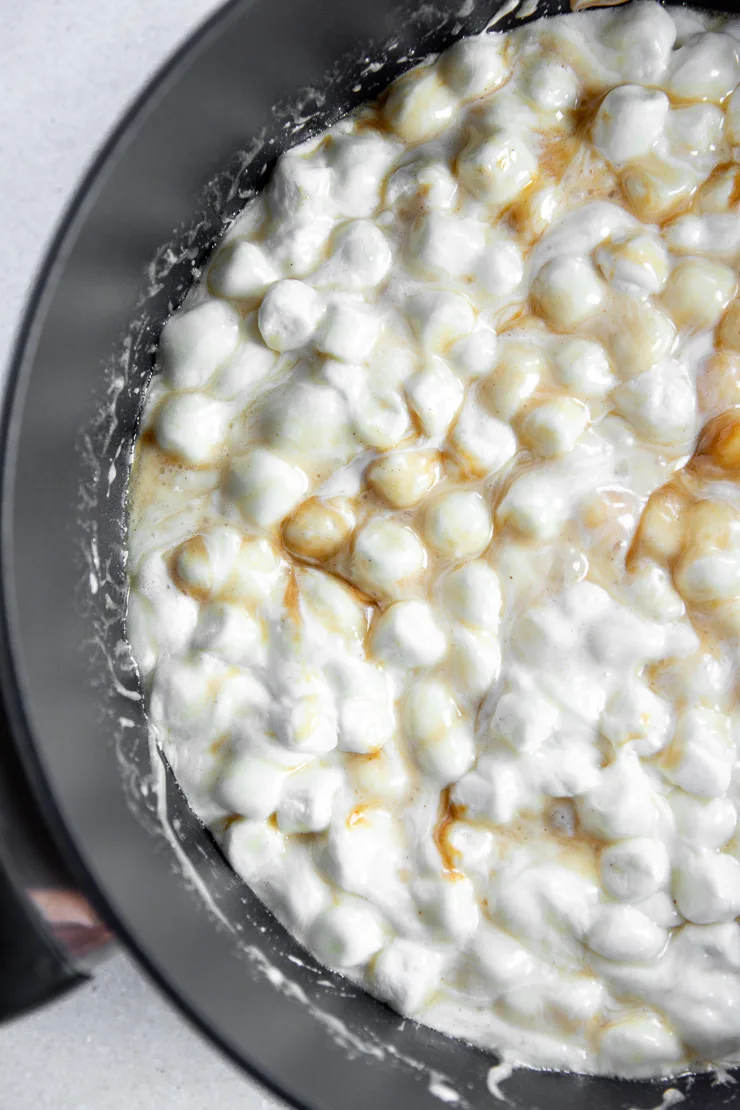 Melty mini marshmallows being stirred into the melted butter mixture with swirls of peanut butter.