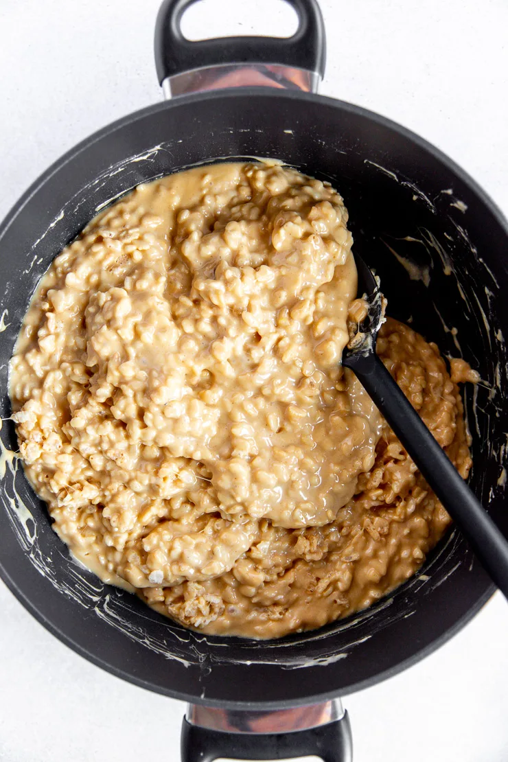 Peanut butter rice krispies being stirred together in a large pot with a black silicone spoon.