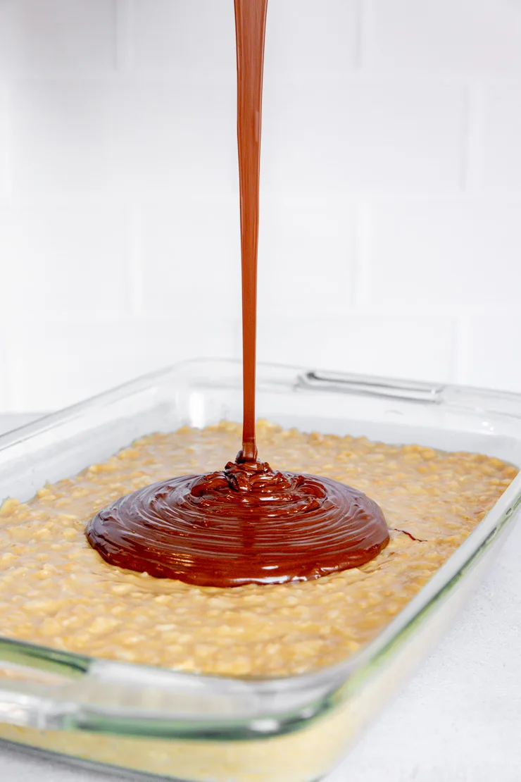 Melted chocolate being poured onto rice krispies treats leaving a melted pile in the middle.