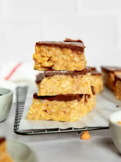 Three stacked scotcharoos on parchment paper in front of a white background.