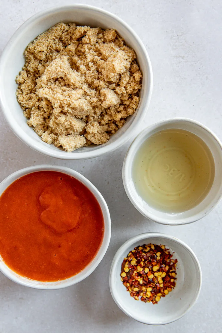 Four small bowls filled with brown sugar, rice vinegar, hot sauce, and crushed red pepper flakes.