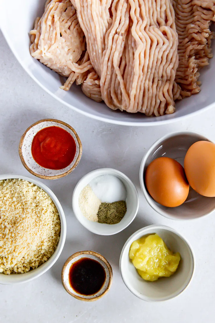 Seven white bowls of various sizes containing each of the ingredients to make firecracker meatballs.