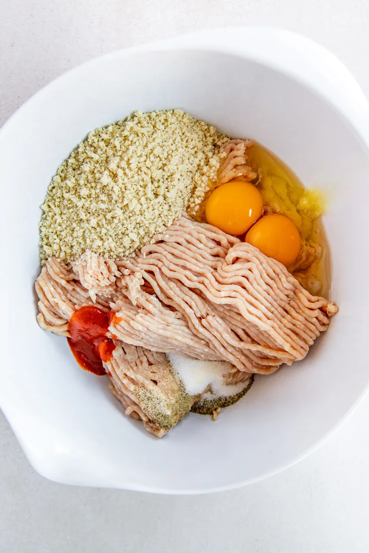 A big white mixing bowl with the firecracker meatball ingredients piled high on top of one another.