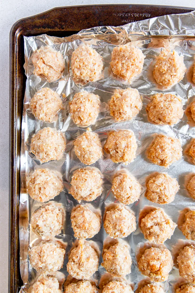 An old cookie sheet with aluminum foil with tightly packed and formed firecracker meatballs waiting to be cooked.