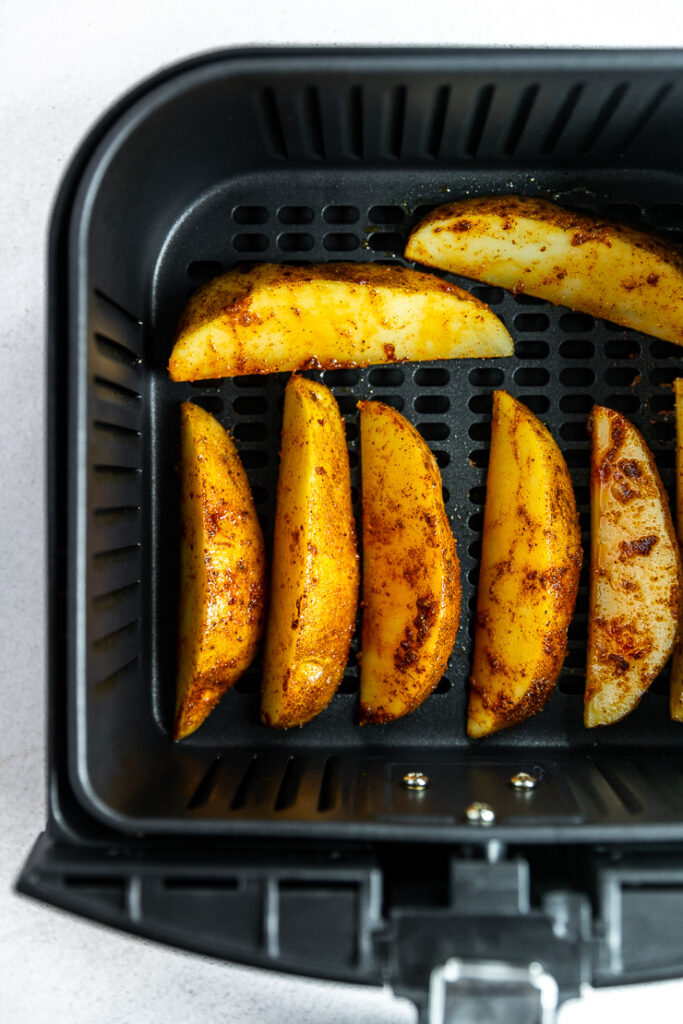 An overhead shot of an air fryer basket with potato wedges laid in a row.