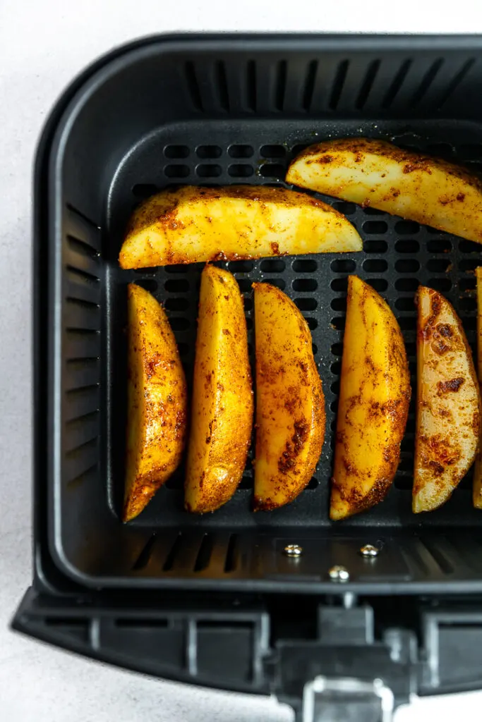 An overhead shot of an air fryer basket with potato wedges laid in a row.