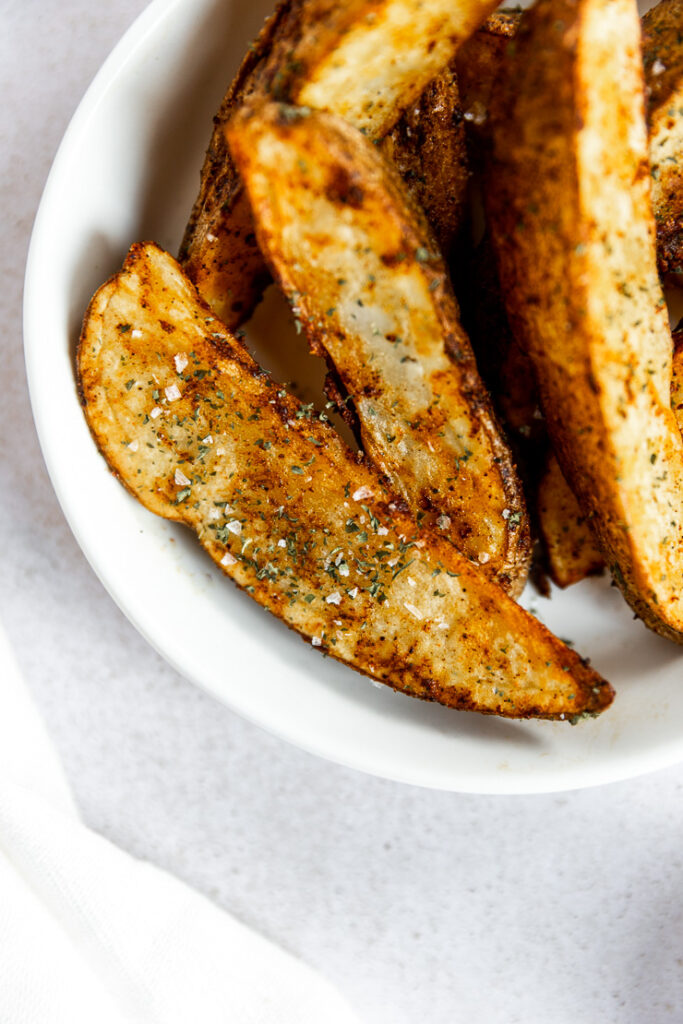 A close up of a cripsy potato wedge covered in seasoning and flaky salt.