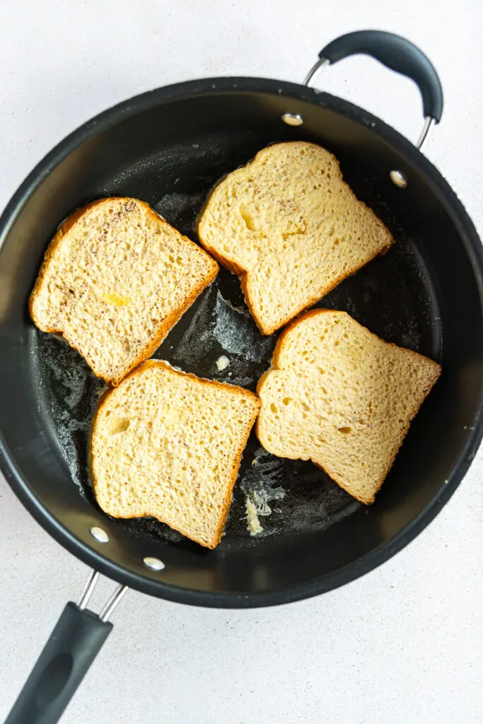 A large saute pan filled with four pieces of french toast in melted butter.