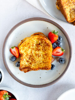 An overhead shot of brioche french toast next to berries on a white plate.