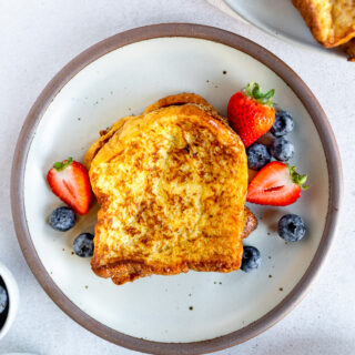 An overhead shot of brioche french toast next to berries on a white plate.