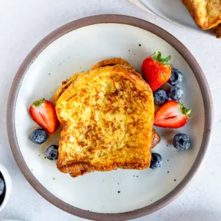An overhead shot of brioche french toast next to berries on a white plate.