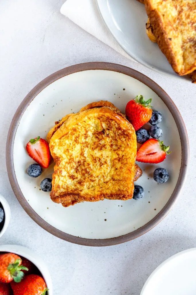An overhead shot of brioche french toast next to berries on a white plate.