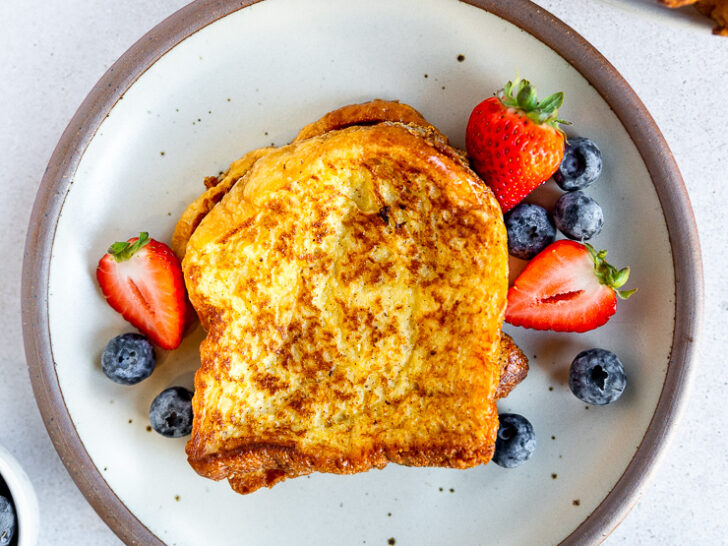 An overhead shot of brioche french toast next to berries on a white plate.