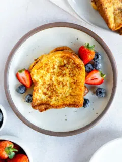 An overhead shot of brioche french toast next to berries on a white plate.