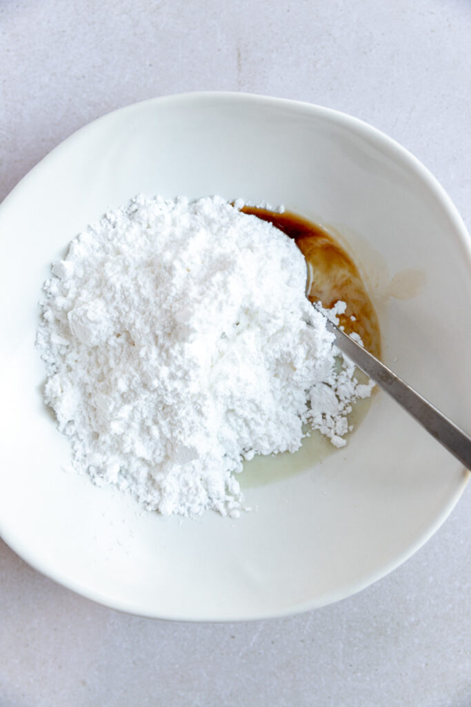 A small white bowl with powdered sugar, vanilla, and milk.