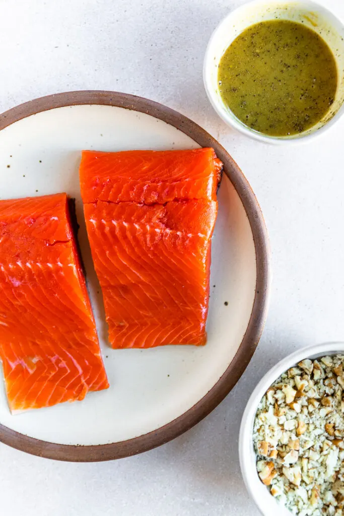 A plate with two salmon filets and two bowls filled with honey mustard and breadcrumbs with diced pecans.