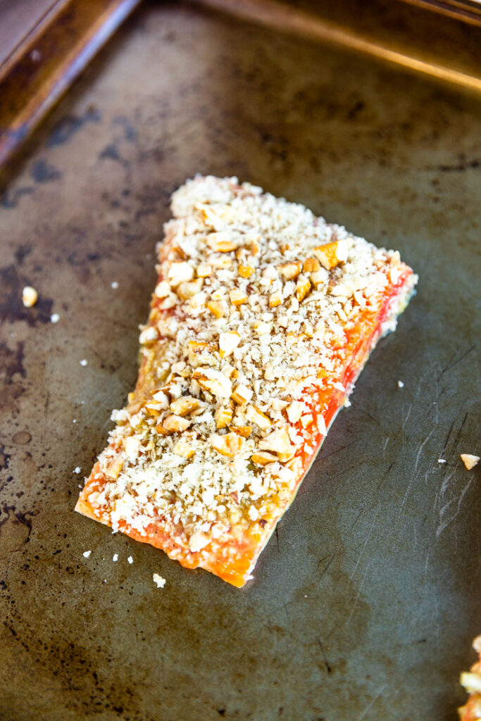 A salmon filet topped with the pecan breadcrumb mixture on a cookie sheet.