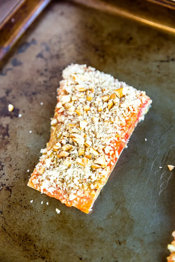 A salmon filet topped with the pecan breadcrumb mixture on a cookie sheet.