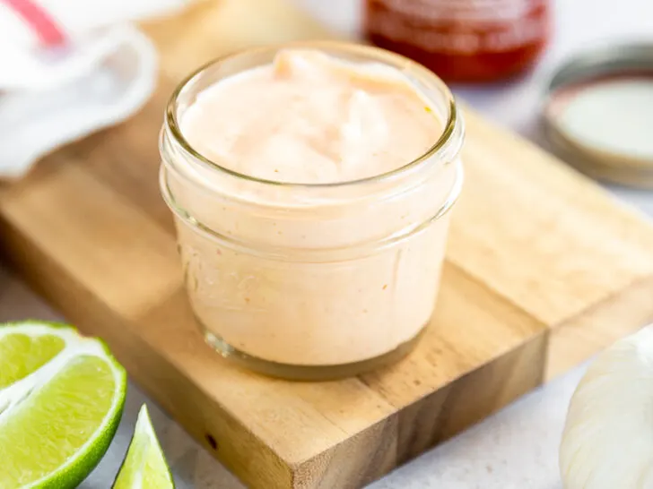 A small mason jar filled with sriracha aioli on a cutting board surrounded by ingredients.