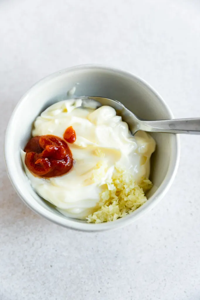 A small white bowl filled with all of the ingredients and a spoon before being stirred.