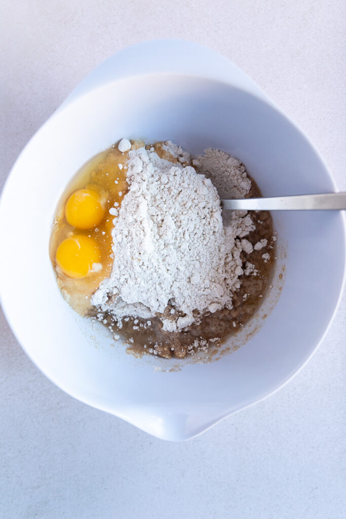 A white mixing bowl with all of the ingredients in the bowl and a metal spoon.