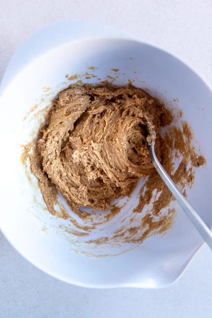 A white mixing bowl with the ingredients mixed into a dough by a metal spoon.