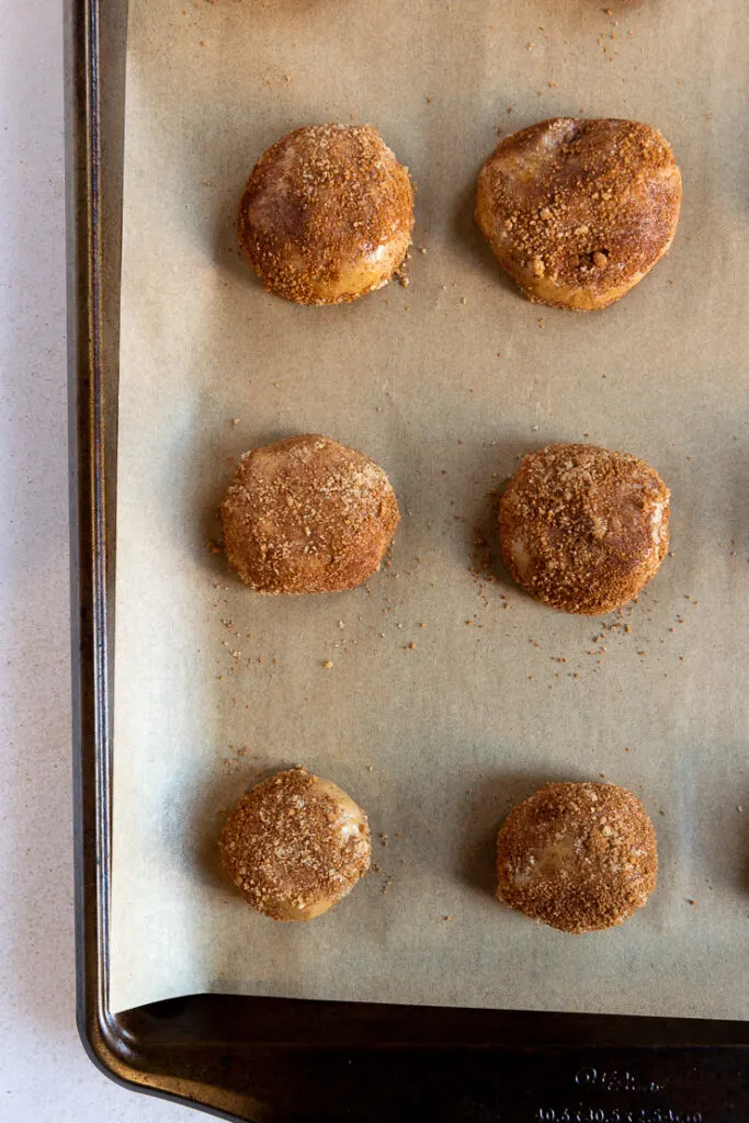 Six dough balls rolled in cinnamon sugar mixture placed on a parchment paper on a cookie sheet.