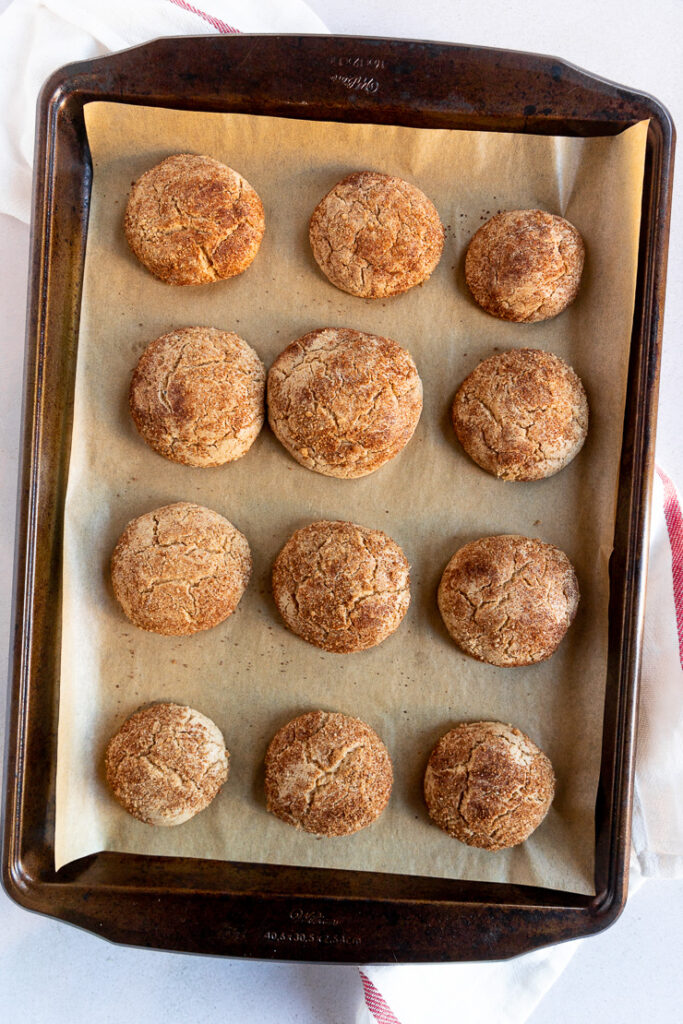 A cookie sheet of baked cookies on top of a white and red striped cloth napkin.