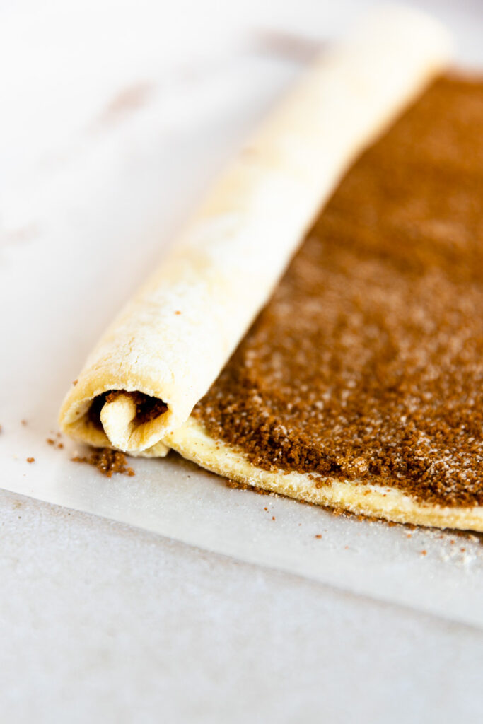 A puff pastry sheet with cinnamon sugar starting to be rolled.