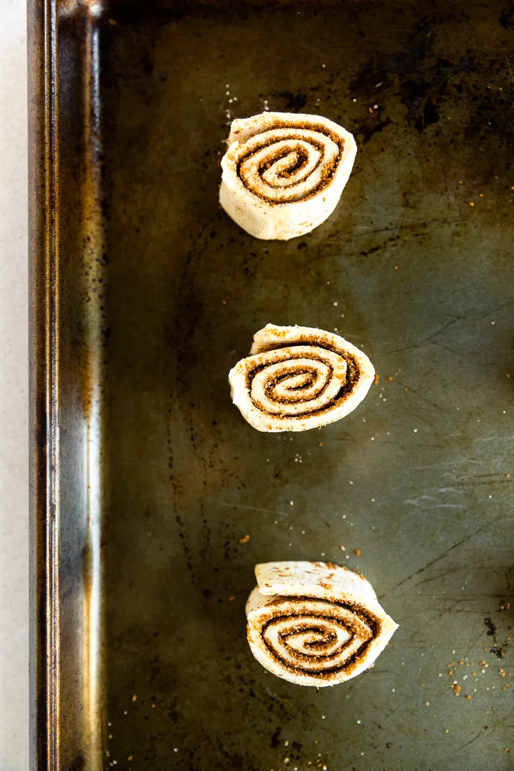 Three raw puff pastry cinnamon rolls on a cookie sheet ready to be baked.