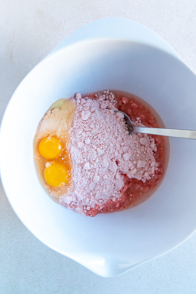 A big white mixing bowl with all of the ingredients in the bottom of the bowl and a big silver spoon sitting in the mixture.