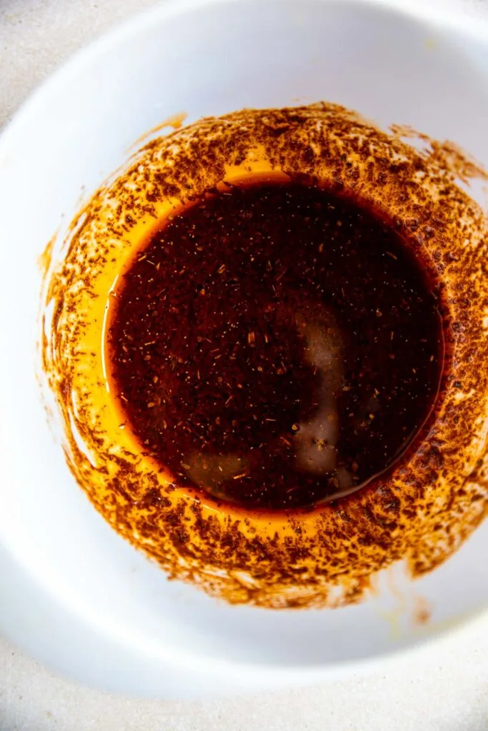 A white bowl containing a reddish-brown ancho marinade, with some of the mixture splattered along the sides of the bowl.