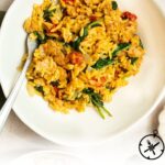A white plate filled with creamy Italian sausage orzo mixed with spinach and sun-dried tomatoes. A fork rests on the plate. The text below reads: Creamy Italian Sausage Orzo. The Culinary Compass.