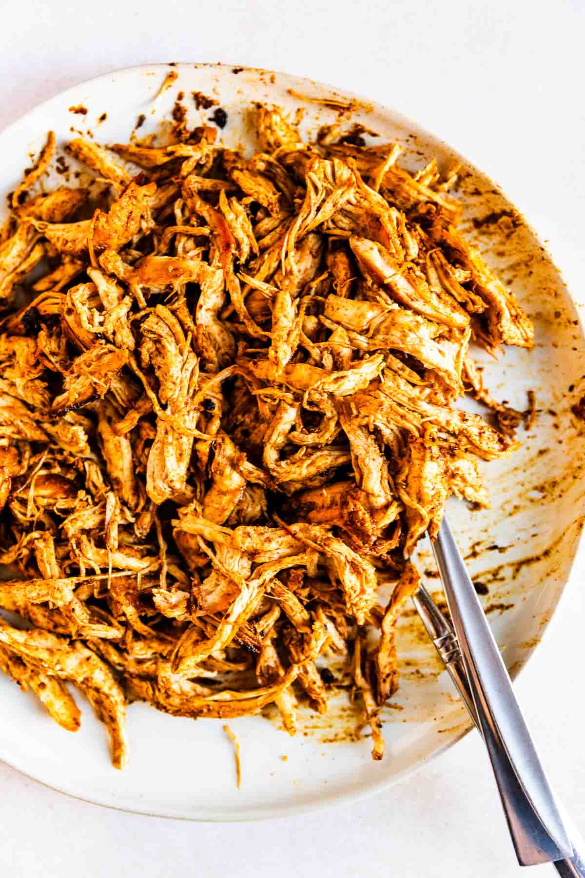 Shredded ancho chile chicken served on a white plate with two forks, displaying a mix of orange and brown spices coating the meat.