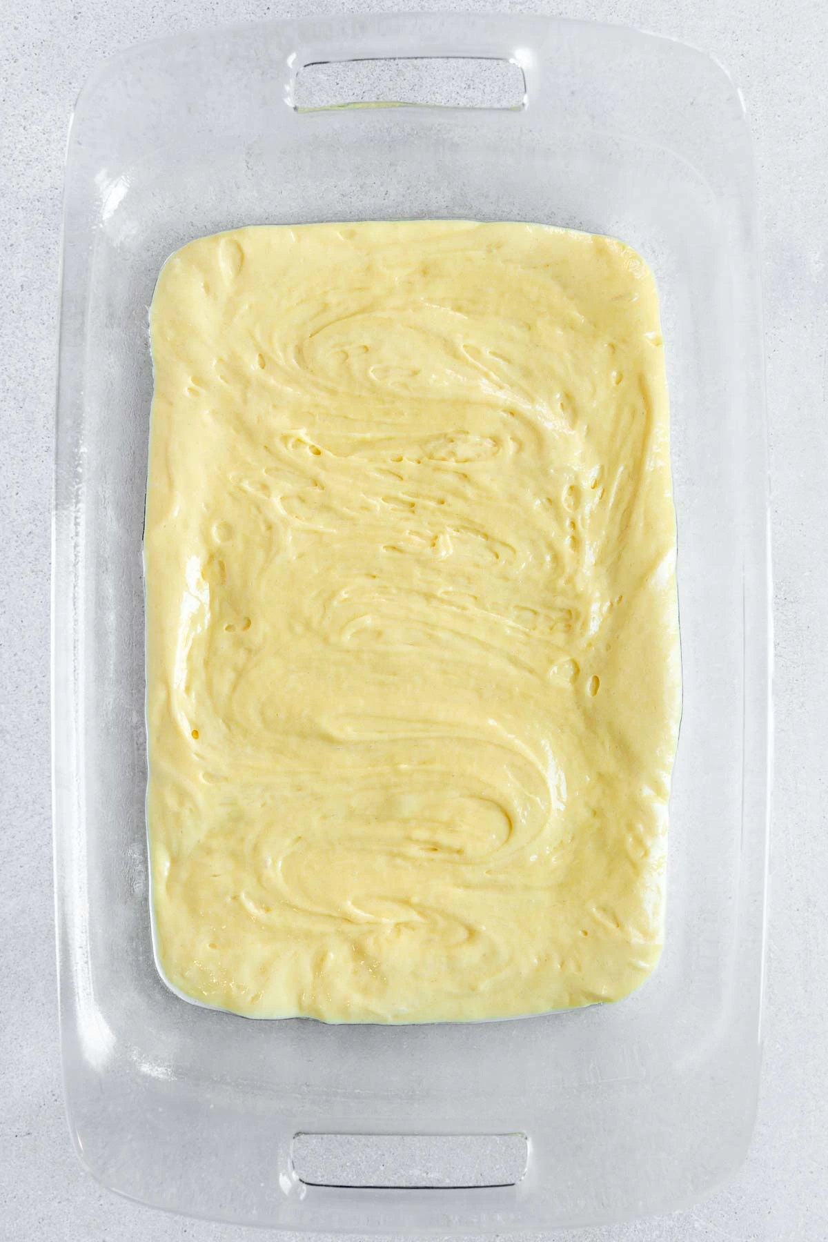 A glass baking dish filled with smooth, swirled yellow cake batter, ready to be baked. The dish is placed on a light-colored surface.