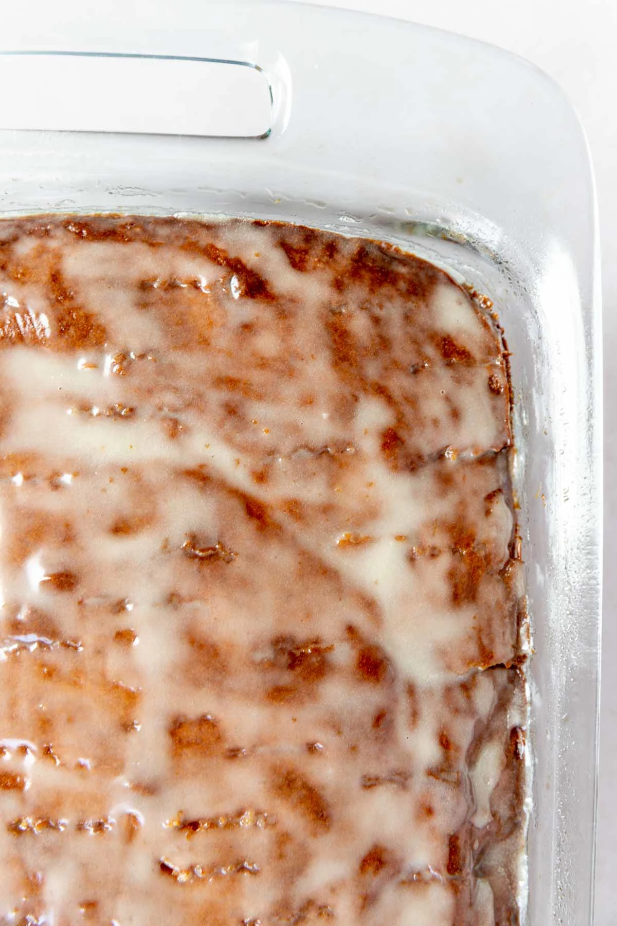 A close-up of a glazed baked cake in a glass pan, showing a shiny layer of icing on the golden-brown surface.