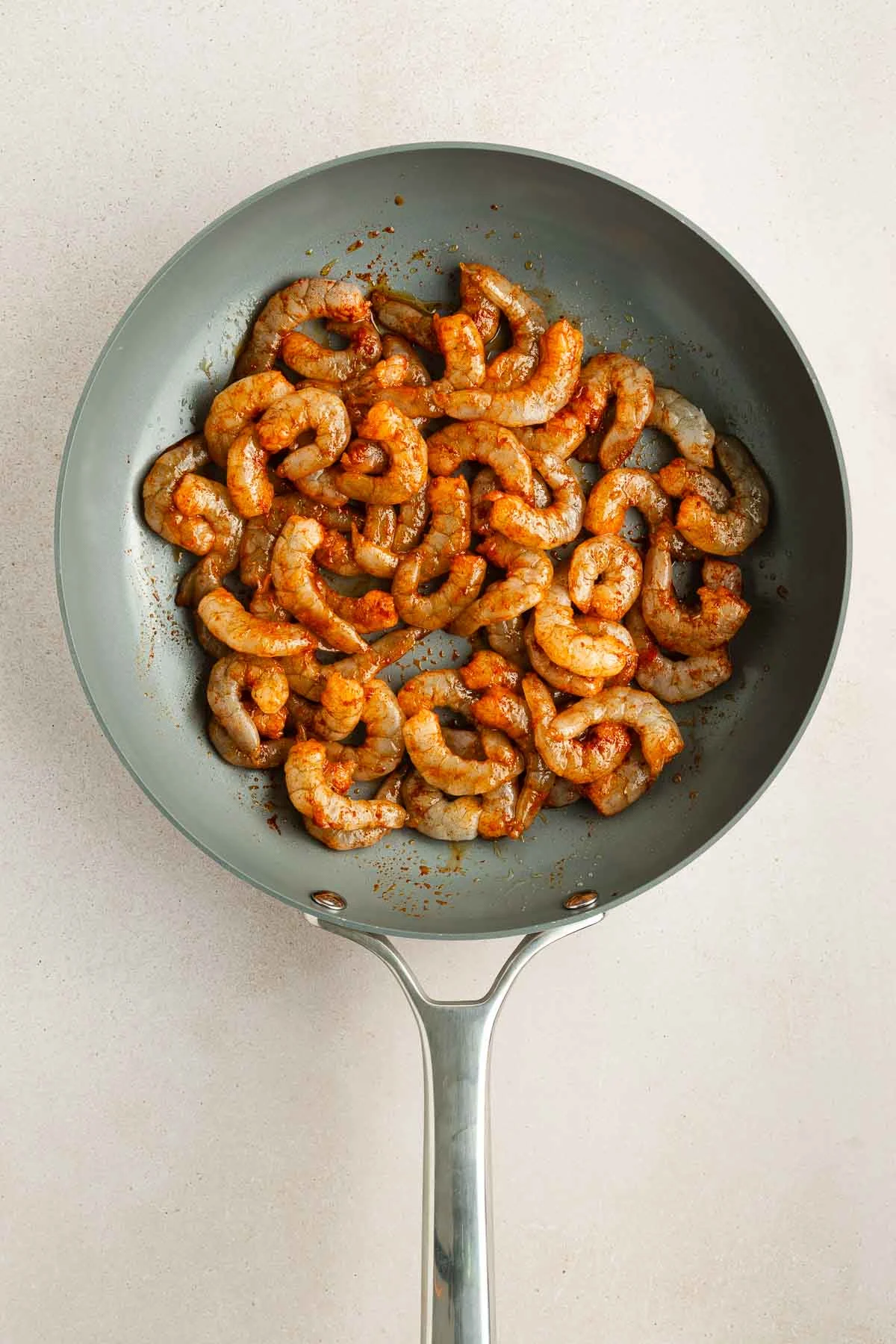 A frying pan with seasoned, raw shrimp arranged in a single layer on a light-colored surface.