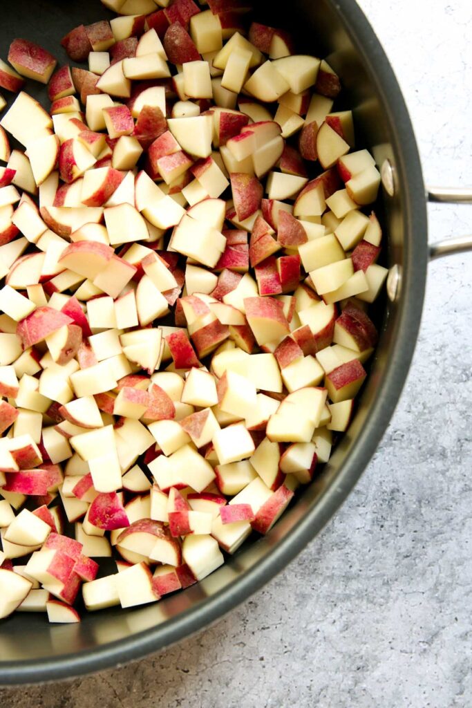 A pan filled with diced red potatoes sits on a light-colored countertop, ready to become crispy skillet breakfast potatoes with their mix of red skin and white potato flesh.