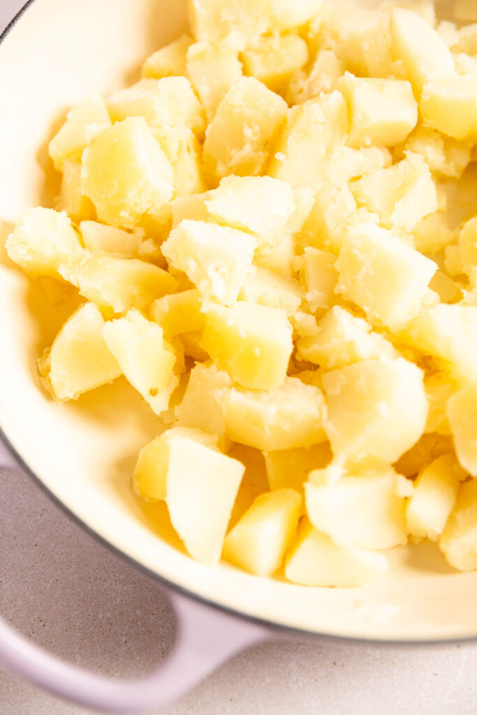 A close-up of chopped, cooked potatoes in a light-colored bowl with a handle, ready to be transformed into flavorful Horseradish Mashed Potatoes for your next recipe.